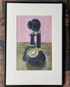 Black old candlestick-style black rotary phone with golden dial and accents against a wooden table and pink background.