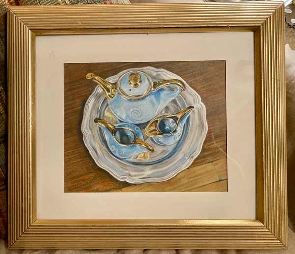 Gold framed drawing of a blue and gold blue porcelain teaset on a silver platter against a wooden table.