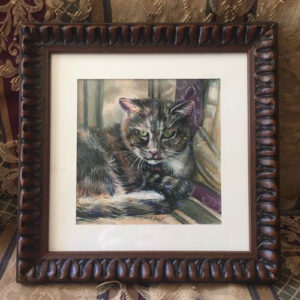 Calico cat in a carved wooden frame.